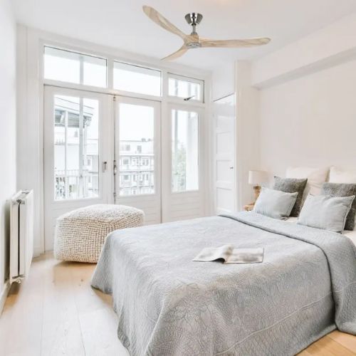Chambre lumineuse et calme avec ventilateur au plafond et lit double, style cocooning, drap gris et coussins, espace frais propice au sommeil. dormir avec un ventilateur allumé la nuit.