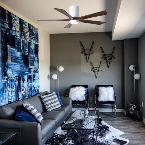 Salon moderne avec ventilateur de plafond, canapé gris et décor noir et blanc, chaise et lampe, ambiance chic et lumineuse.